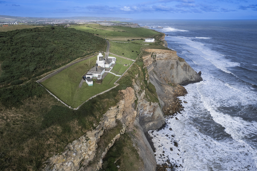 Aerial view of Whitby Lighthouse perched on the dramatic coastal cliffs overlooking the North Sea with green fields and rugged rock formations in Whitby England United Kingdom. Aerial view of Whitby Lighthouse perched on the dramatic coastal cliffs overlooking the North Sea with green fields and rugged rock formations in Whitby England United Kingdom.