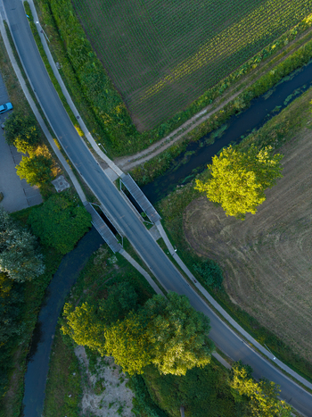 Aerial view of a road bridge crossing a small stream surrounded by lush green fields trees and rural landscape in Hasselt Flanders Belgium. Aerial view of a road bridge crossing a small stream surrounded by lush green fields trees and rural landscape in Hasselt Flanders Belgium.