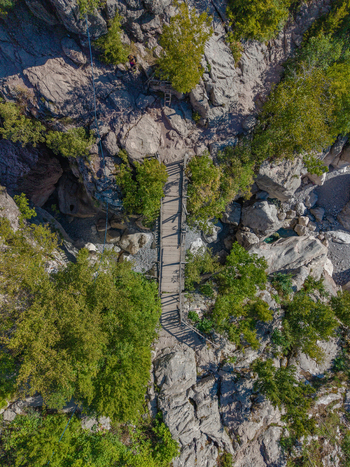Aerial view of the wooden bridge crossing the rocky terrain near the Blue eye Theth surrounded by lush green forest in Theth Shkoder County Albania. Aerial view of the wooden bridge crossing the rocky terrain near the Blue eye Theth surrounded by lush green forest in Theth Shkoder County Albania.