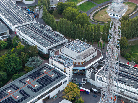 Aerial view of Messe Berlin exhibition grounds featuring the iconic Funkturm radio tower modern exhibition halls with solar panels and surrounding green spaces in Berlin Berlin Germany. Aerial view of Messe Berlin exhibition grounds featuring the iconic Funkturm radio tower modern exhibition halls with solar panels and surrounding green spaces in Berlin Berlin Germany.