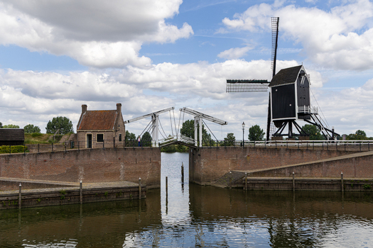 View of a traditional Dutch windmill and a historic drawbridge over a canal with brick fortifications in Heusden North Brabant Netherlands.