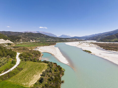 Aerial view of Vjosa Wild River National Park with its turquoise river gravel banks and surrounding green hills under a clear blue sky in Permet Gjirokaster County Albania. Aerial view of Vjosa Wild River National Park with its turquoise river gravel banks and surrounding green hills under a clear blue sky in Permet Gjirokaster County Albania.