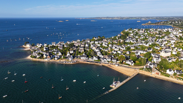 Aerial view of a quaint coastal town with boats dotting the shimmering water and a long pier stretching into the sea Carantec France.