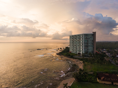 Aerial view of Gintota beach and a modern high rise building during a golden sunset with light reflecting on the ocean waves and palm trees in Galle Southern Province Sri Lanka. Aerial view of Gintota beach and a modern high rise building during a golden sunset with light reflecting on the ocean waves and palm trees in Galle Southern Province Sri Lanka.