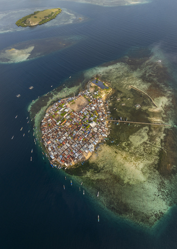 Aerial view of Pulau Mesa island with its densely packed houses wooden piers and surrounding coral reefs in the clear blue waters of Kecamatan Komodo Nusa Tenggara Timur Indonesia. Aerial view of Pulau Mesa island with its densely packed houses wooden piers and surrounding coral reefs in the clear blue waters of Kecamatan Komodo Nusa Tenggara Timur Indonesia.