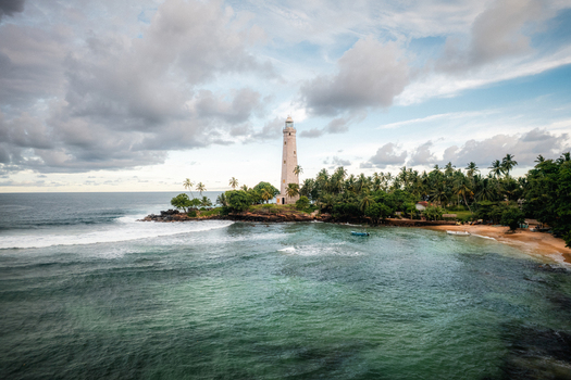 Aerial view of Dondra Lighthouse surrounded by lush palm trees and rocky coastline with turquoise ocean waves crashing against the shore in Dondra Southern Province Sri Lanka. Aerial view of Dondra Lighthouse surrounded by lush palm trees and rocky coastline with turquoise ocean waves crashing against the shore in Dondra Southern Province Sri Lanka.