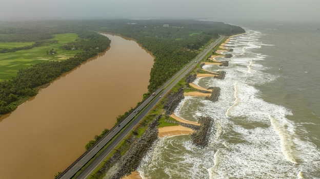 Aerial view of Maravanthe beach where the Arabian Sea meets the Suparnika River separated by a highway with waves crashing against stone breakwaters in Maravanthe Karnataka India. Aerial view of Maravanthe beach where the Arabian Sea meets the Suparnika River separated by a highway with waves crashing against stone breakwaters in Maravanthe Karnataka India.