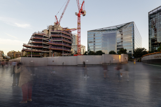 View of The Scoop with a construction site a red crane and a modern glass office building with people walking in the foreground London England United Kingdom. View of The Scoop with a construction site a red crane and a modern glass office building with people walking in the foreground London England United Kingdom.