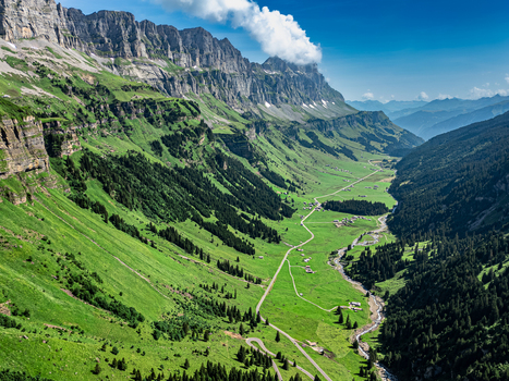 Aerial view of a lush valley floor framed by towering cliffs under a bright sky Spiringen Uri Switzerland. Aerial view of a lush valley floor framed by towering cliffs under a bright sky Spiringen Uri Switzerland.