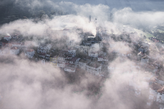 Aerial view of the historic village of Avo shrouded in thick morning fog and mist with traditional white houses and red tiled roofs Oliveira do Hospital Coimbra District Portugal.