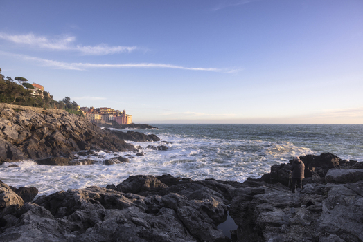 View of the historic village of Tellaro perched on the rocky coastline with crashing waves and a person standing on the shore during golden hour in Tellaro Liguria Italy. View of the historic village of Tellaro perched on the rocky coastline with crashing waves and a person standing on the shore during golden hour in Tellaro Liguria Italy.