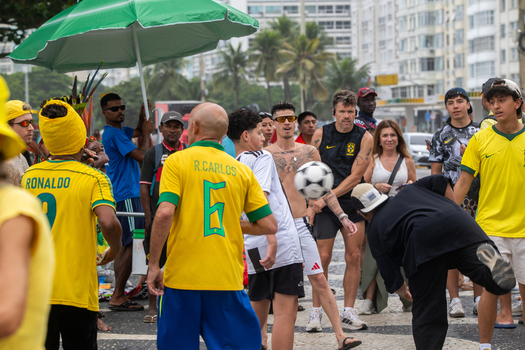 Rio de Janeiro Brazil 13 June 2026 View of football fans in Brazil jerseys playing with a ball on the sidewalk near the beach with buildings and palm trees in the background.