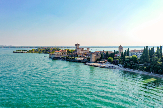 Aerial view of Castello Scaligero di Sirmione a historic fortress on the shores of Lake Garda with turquoise waters and lush green trees Sirmione Lombardia Italy.