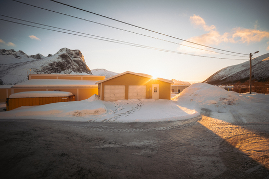 View of the golden sun casting long shadows across snow covered ground and buildings with a mountain backdrop Indregård Troms Norway. View of the golden sun casting long shadows across snow covered ground and buildings with a mountain backdrop Indregård Troms Norway.