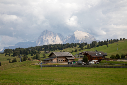 View of traditional wooden chalets nestled in lush green meadows with the majestic peaks of the Dolomites under a cloudy sky in Rocca Pietore Veneto Italy. View of traditional wooden chalets nestled in lush green meadows with the majestic peaks of the Dolomites under a cloudy sky in Rocca Pietore Veneto Italy.