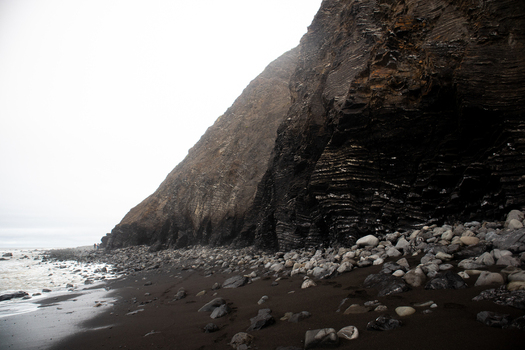 View of the rugged cliffs and black sand beach at the Lost Coast with geological rock layers and smooth stones Humboldt County California United States.