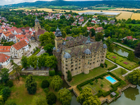 Aerial view of the historic Neuenstein Castle surrounded by lush gardens a moat and the charming town of Neuenstein Baden Wurttemberg Germany. Aerial view of the historic Neuenstein Castle surrounded by lush gardens a moat and the charming town of Neuenstein Baden Wurttemberg Germany.