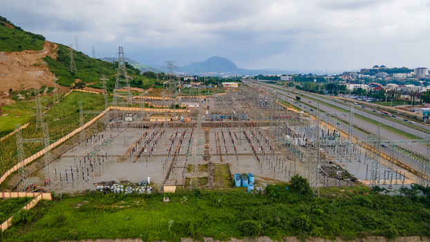 Aerial view of TCN SubStation Katampe featuring electrical transformers power lines and metal structures near a highway with green hills in Abuja Federal Capital Territory Nigeria.