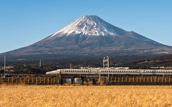 View of a Shinkansen bullet train passing through the countryside with the snow capped Mount Fuji in the background under a clear blue sky in Fujinomiya Shizuoka Japan. View of a Shinkansen bullet train passing through the countryside with the snow capped Mount Fuji in the background under a clear blue sky in Fujinomiya Shizuoka Japan.