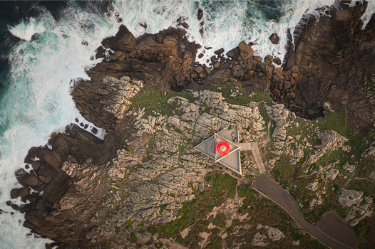 Aerial view of the Faro de Punta Nariga lighthouse with its unique triangular shape situated on rugged rocky cliffs as waves crash against the shore in Malpica A Coruna Spain. Aerial view of the Faro de Punta Nariga lighthouse with its unique triangular shape situated on rugged rocky cliffs as waves crash against the shore in Malpica A Coruna Spain.