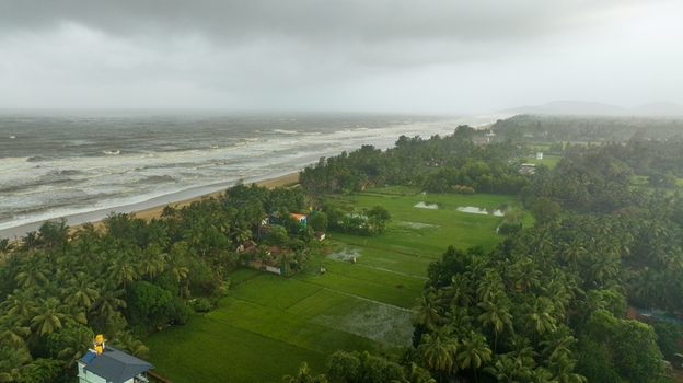 Aerial view of Gokarna beach with lush green rice paddies and palm trees under a stormy sky in Gokarna Karnataka India.