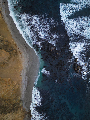 Aerial view of the Reserva Nacional de Paracas with white waves crashing against the sandy shore and rugged cliffs in Paracas Ica Peru.
