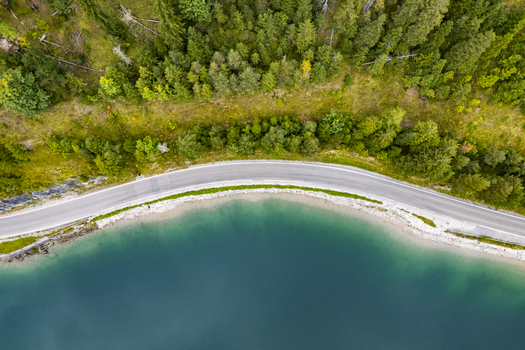 Aerial view of the road curving along the turquoise Plansee lake under a dense green forest canopy Plansee Tyrol Austria. Aerial view of the road curving along the turquoise Plansee lake under a dense green forest canopy Plansee Tyrol Austria.