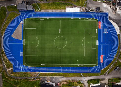 Aerial view of Djupumyra Stadium featuring a green football pitch and a vibrant blue running track with people in Klaksvik Northern Isles Faroe Islands.