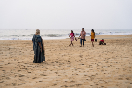 Sri Lanka 20 January 2026 View of people walking and playing on a sandy beach with ocean waves under a hazy sky.