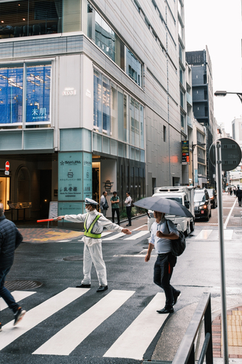 Tokyo Japan 01 October 2025 View of a crossing guard directing traffic on a zebra crossing framed by the sleek architecture and the muted tones of a bustling city street. Tokyo Japan 01 October 2025 View of a crossing guard directing traffic on a zebra crossing framed by the sleek architecture and the muted tones of a bustling city street.