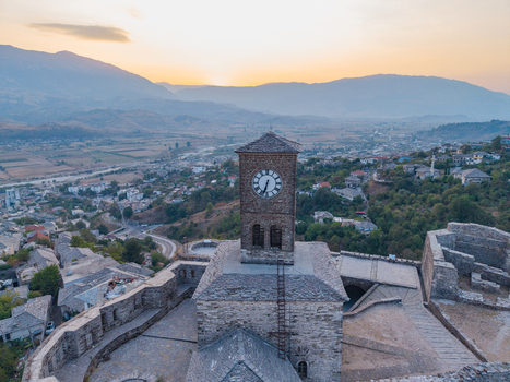 Aerial view of the historic clock tower at Gjirokaster Fortress surrounded by stone walls and the scenic valley landscape at sunset in Gjirokaster Gjirokaster County Albania. Aerial view of the historic clock tower at Gjirokaster Fortress surrounded by stone walls and the scenic valley landscape at sunset in Gjirokaster Gjirokaster County Albania.