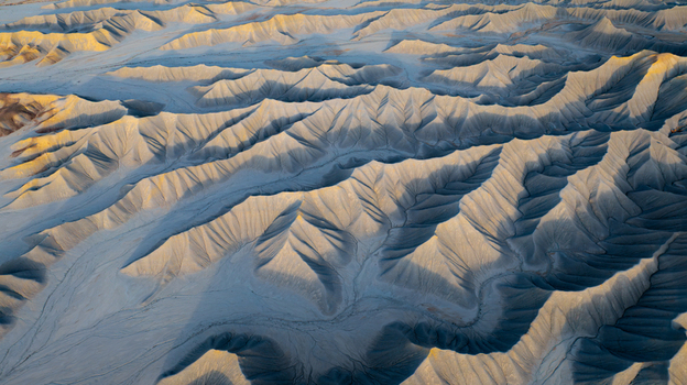 Aerial view of the badlands in Hanksville featuring intricate eroded ridges deep gullies and golden light hitting the desert landscape. Hanksville Utah United States.