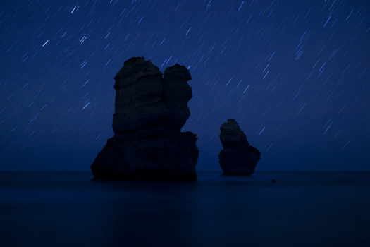 View of limestone stacks silhouetted against a deep blue night sky with star trails over the ocean at Twelve Apostles Marine National Park Australia. View of limestone stacks silhouetted against a deep blue night sky with star trails over the ocean at Twelve Apostles Marine National Park Australia.