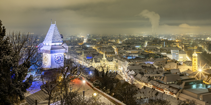 View of illuminated clock tower standing proudly amidst a snow dusted cityscape under a night sky its face glowing warmly Graz Styria Austria. View of illuminated clock tower standing proudly amidst a snow dusted cityscape under a night sky its face glowing warmly Graz Styria Austria.