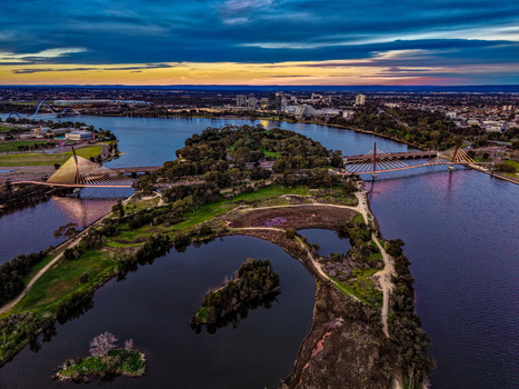Aerial view of Boorloo Bridge spanning the Swan River with lush parkland and the urban skyline under a vibrant sunset sky in East Perth Western Australia Australia.