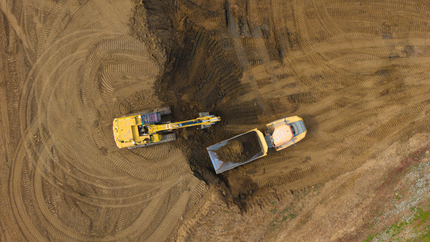 Aerial view of an excavator loading soil into a dump truck at the Black Cat Roundabout construction site in Chawston England United Kingdom. Aerial view of an excavator loading soil into a dump truck at the Black Cat Roundabout construction site in Chawston England United Kingdom.
