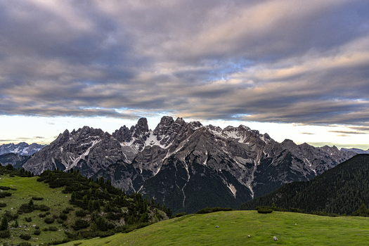 View of the jagged peaks of the Dolomites from the green alpine meadows of Prato Piazza under a dramatic cloudy sky in Dobbiaco Trentino Alto Adige Italy. View of the jagged peaks of the Dolomites from the green alpine meadows of Prato Piazza under a dramatic cloudy sky in Dobbiaco Trentino Alto Adige Italy.