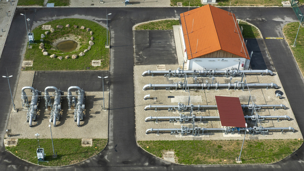Aerial view of a gas pressure regulation station with industrial piping valves and a small utility building with an orange roof in Finsing Bavaria Germany.