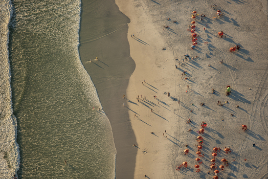 Aerial view of the sandy beach in Rio de Janeiro with people relaxing under orange umbrellas near the Atlantic Ocean in Rio de Janeiro Rio de Janeiro Brazil. Aerial view of the sandy beach in Rio de Janeiro with people relaxing under orange umbrellas near the Atlantic Ocean in Rio de Janeiro Rio de Janeiro Brazil.