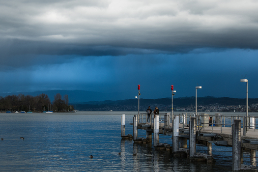 Zurich Switzerland 02 April 2023 View of a pier stretching into the shimmering lake under a stormy sky where the dark clouds meet the serene water. Zurich Switzerland 02 April 2023 View of a pier stretching into the shimmering lake under a stormy sky where the dark clouds meet the serene water.