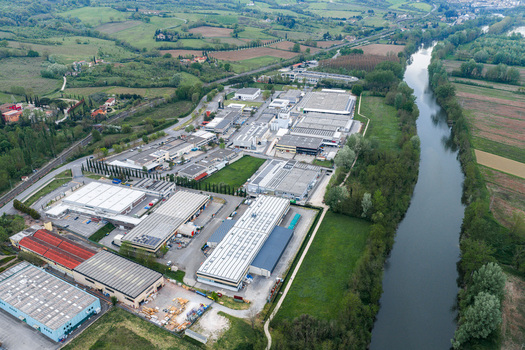 Aerial view of industrial warehouses and commercial buildings situated along a winding river surrounded by green fields and rolling hills in Leccio Toscana Italy. Aerial view of industrial warehouses and commercial buildings situated along a winding river surrounded by green fields and rolling hills in Leccio Toscana Italy.