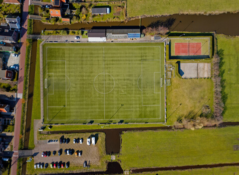 Aerial view of the vibrant green football field contrasted against the surrounding brown brick buildings and the red tennis court Oostknollendam Netherlands. Aerial view of the vibrant green football field contrasted against the surrounding brown brick buildings and the red tennis court Oostknollendam Netherlands.