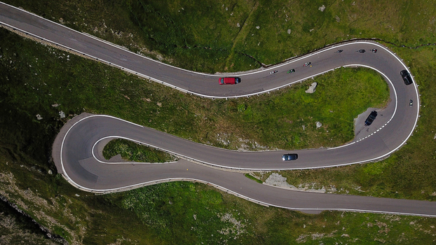 Aerial view of the winding Furka Pass mountain road with hairpin turns and cars driving through green alpine slopes in Obergoms Valais Switzerland. Aerial view of the winding Furka Pass mountain road with hairpin turns and cars driving through green alpine slopes in Obergoms Valais Switzerland.