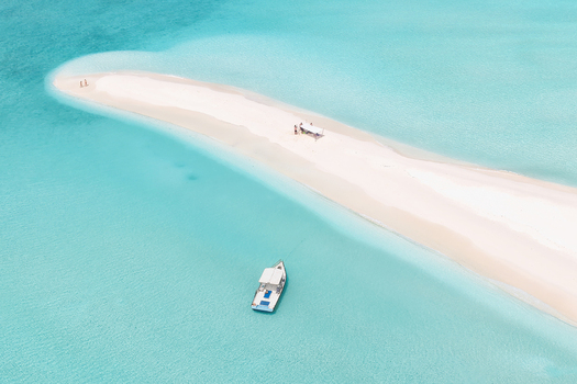 Aerial view of a pristine white sandbar surrounded by crystal clear turquoise water with a small boat and people on the beach in Vashafaru Haa Alif Atoll Maldives. Aerial view of a pristine white sandbar surrounded by crystal clear turquoise water with a small boat and people on the beach in Vashafaru Haa Alif Atoll Maldives.