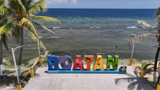 Aerial view of the colorful Roatan sign on a concrete platform overlooking the Caribbean sea with palm trees on both sides in West End Bay Islands Department Honduras. Aerial view of the colorful Roatan sign on a concrete platform overlooking the Caribbean sea with palm trees on both sides in West End Bay Islands Department Honduras.