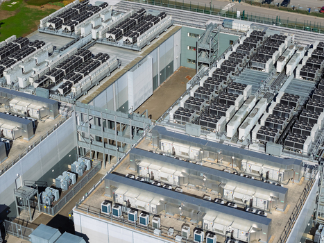 Aerial view of a large data center facility featuring rows of industrial HVAC cooling units on the roof metallic structures and paved service areas in the United Kingdom.