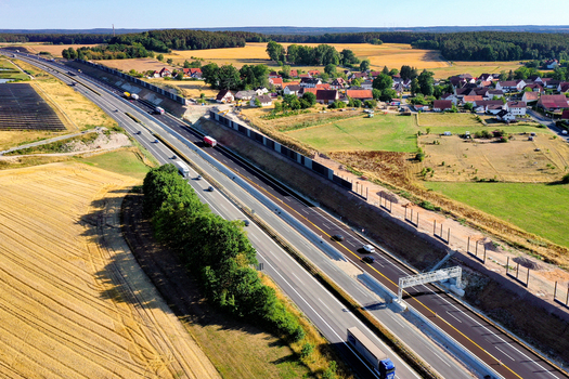 Nurnberg Germany 18 May 2024 Aerial view of the A73 highway with traffic passing through sound barriers next to a small village and golden wheat fields. Nurnberg Germany 18 May 2024 Aerial view of the A73 highway with traffic passing through sound barriers next to a small village and golden wheat fields.