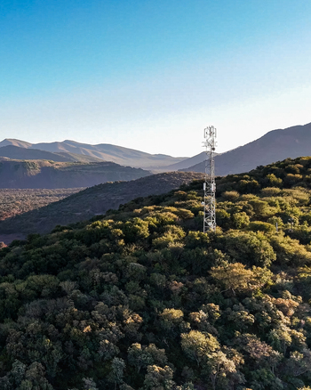 Aerial view of a communication tower standing on a lush tree covered hillside under a clear blue sky in Rustenburg North West South Africa.
