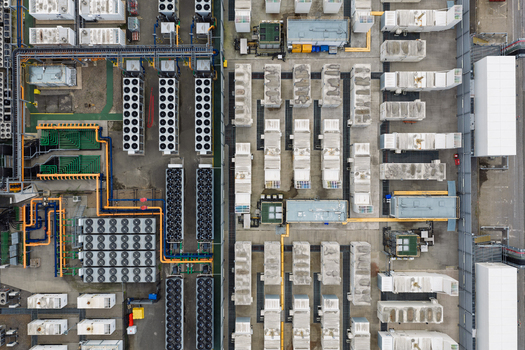 Aerial view of a data center featuring rows of server containers industrial cooling units and complex piping systems in the United Kingdom.