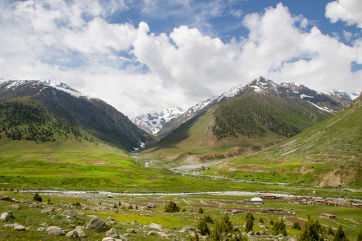 View of the lush green Astore Valley with snow capped mountain peaks a winding river and scattered rural houses under a cloudy sky Astore Gilgit Pakistan. View of the lush green Astore Valley with snow capped mountain peaks a winding river and scattered rural houses under a cloudy sky Astore Gilgit Pakistan.